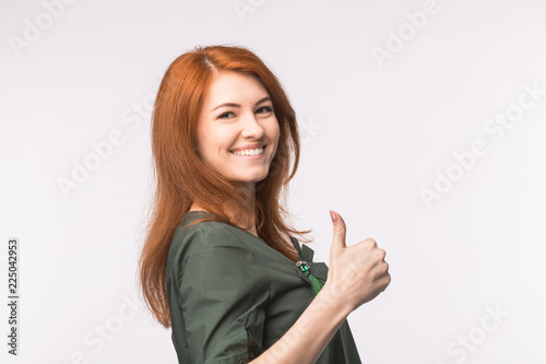 Happy young red-haired woman showing thumb up on white background.