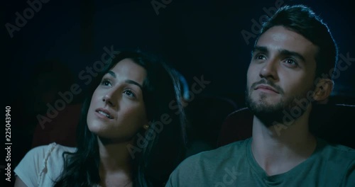 Young dating couple at the movie theatre. Slow tracking shot around them
