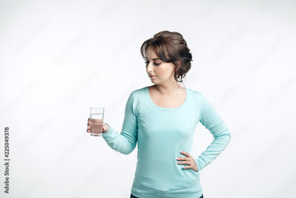 A young brown-haired woman in a mint-colored jumper holding a glass of clean water and looking on it. A young brown-haired woman in a mint-colored jumper holding a glass of clean water and looking on it.