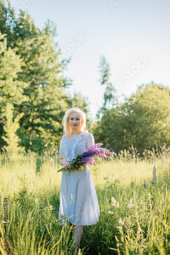 Beautiful young girl in the flowers of lupine. Girl with blonde hair in a long dress with a bouquet of flowers