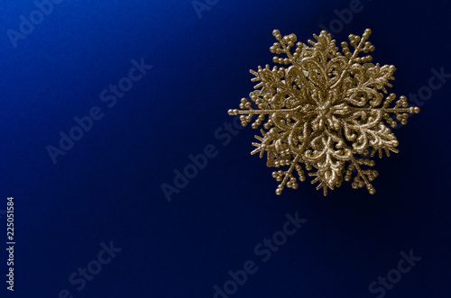 Close-up of a decorative golden snowflake on the up-right corner of a blue gradient background. Light from up-left corner