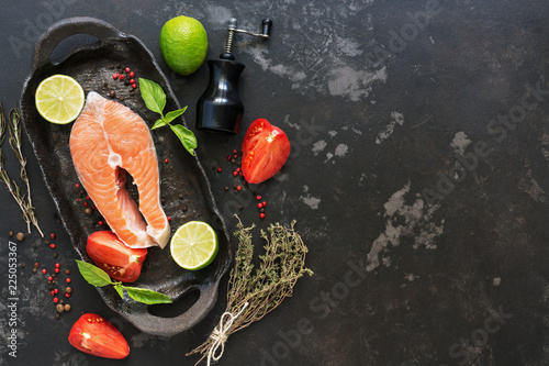 Salmon steak raw with ingredients for cooking on a black stone background. Top view, copy space.