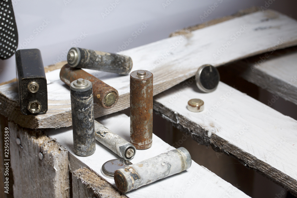 Used finger-wound batteries covered with corrosion. They lie on a wooden box. Next working gloves. Recycling. Used finger-wound batteries covered with corrosion. They lie on a wooden box. Next working gloves. Recycling.