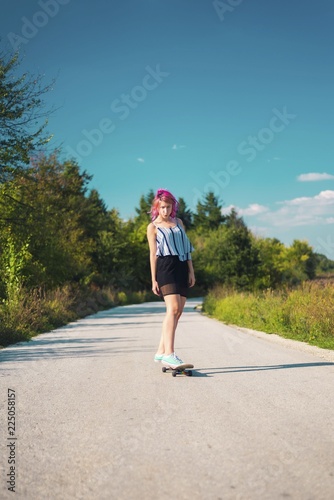 Pink haired young woman skateboarding in nature