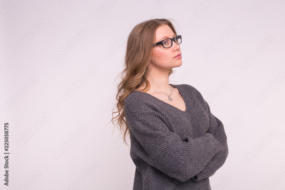 Emotions and people concept - Young woman on a white background with copy space in a grey knitting sweater hugging herself looking at camera