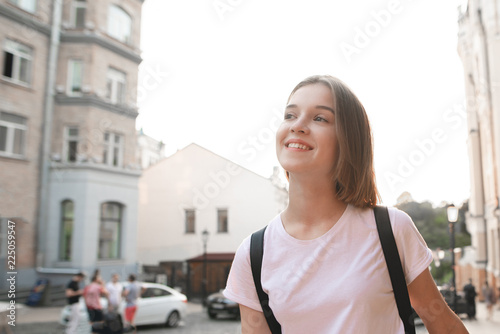 Free Download Smiling, attractive girl walks around the town at sunset and looks to the side. Close-up portrait of a cute young woman in a white T-shirt while walking. - GFXLoad