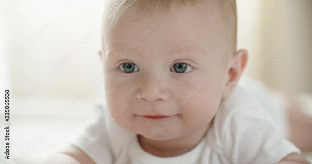 A cute happy baby lying on white bed sheet, looking around and happily laughing and smiling. closeup 4k A cute happy baby lying on white bed sheet, looking around and happily laughing and smiling. closeup 4k