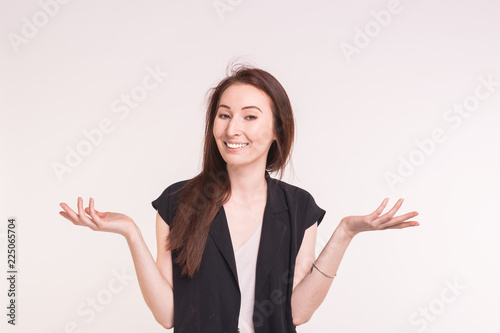 Young brunette asian woman is shrugging her shoulders on white background.