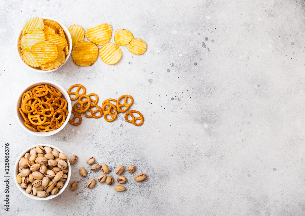 Pretzel and potato crisps and pistachio in white ceramic bowl on stone kitchen table background. Space for text. Snack for beer Pretzel and potato crisps and pistachio in white ceramic bowl on stone kitchen table background. Space for text. Snack for beer