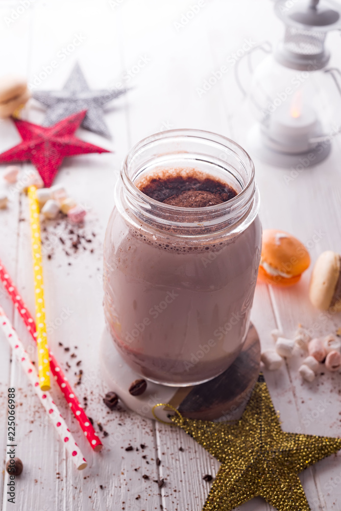 Cocoa with marshmallow and straws in the glass jar decorated with christmas stars on the wooden white table for the winter holidays Cocoa with marshmallow and straws in the glass jar decorated with christmas stars on the wooden white table for the winter holidays