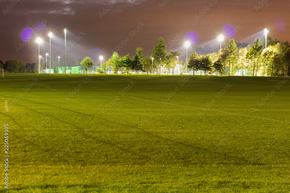 A grass field near a football pitch artificially illuminated late at night. A grass field near a football pitch artificially illuminated late at night.