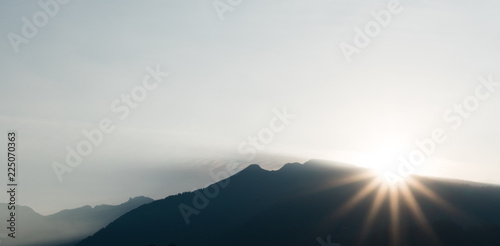 panorama view of a mountain landscape in silhouette with the sun setting