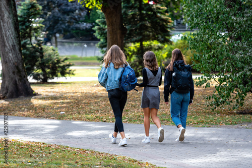 Fototapeta Naklejka Na Ścianę i Meble -  Three girls with a backpack walking along the city park.