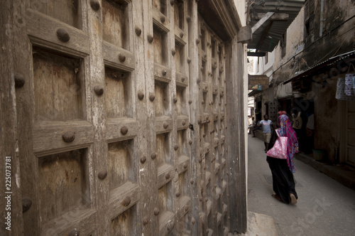 Zanzibar - Tanzania  30 August 2018 - typical Zanzibar town street with old wood doors and woman walking away, Africa