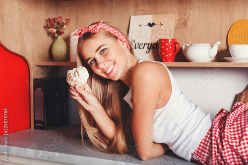 Pretty blonde long hair woman laying on the table, smiling and holding cupcake in the red loft comfortable kitchen photo