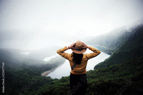 woman traveler holding hat and looking at amazing mountains and forest, wanderlust travel concept, space for text, atmospheric epic moment, azores ,portuhal, ponta delgada, sao miguel