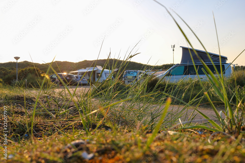 Grass growing next to a raod, leading through a campground in the dunes of northern holland. Campers, caravans and cars standing on the camping pitches in the background
