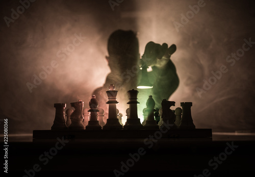 Man playing chess. Scary blurred silhouette of a person at the chessboard with chess figures. Dark toned foggy background. photo