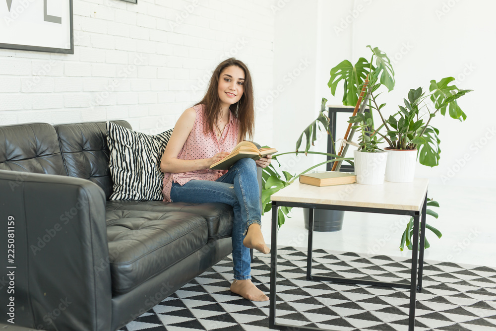 Education and people concept - young woman sitting on the sofa with book Education and people concept - young woman sitting on the sofa with book