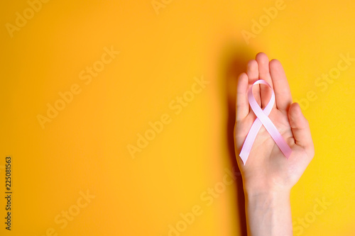 Woman hands holding pink colored ribbon - international symbol of breast cancer awareness and moral support for illness survivors. Isolated background  copy space  close up  top view fat lay.