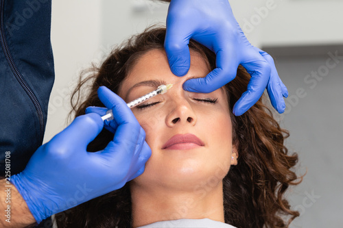 Close up of beautician expert's hands injecting botox in female forehead. photo