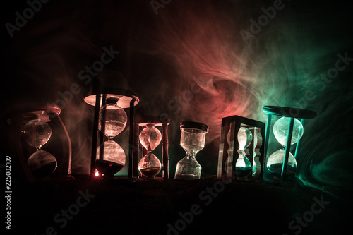 Time concept. Silhouette of Hourglass clock and smoke on dark background with hot yellow orange red blue cold back lighting