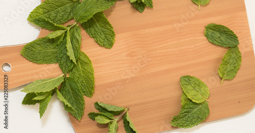 Fresh green mint leaves are on edge of a wooden cutting board. Place in the middle of board is free for your words. View from above.