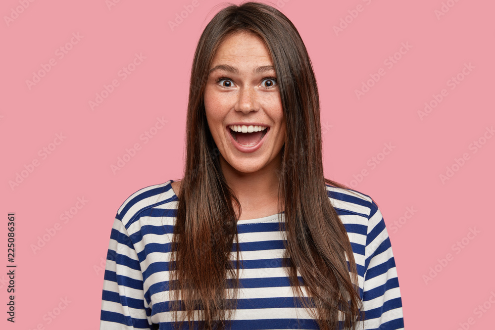 Photo of beautiful lady enjoys life, laughs positively, being amused by funny joke, wears striped casual jacket, models against pink studio wall, recieves pleasant gift, enjoys success and wealth Photo of beautiful lady enjoys life, laughs positively, being amused by funny joke, wears striped casual jacket, models against pink studio wall, recieves pleasant gift, enjoys success and wealth