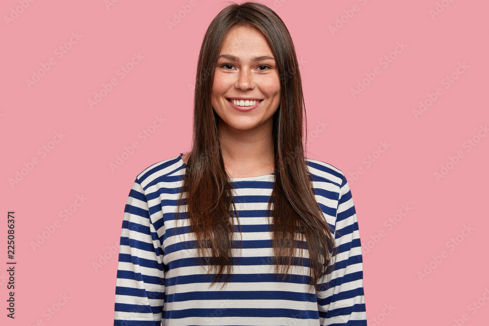 Positive emotions and feelings, happiness concept. Satisfied woman adult smiles joyfully, being glad to recieve new job position or good proposal, dressed in sailor jacket, models indoor alone.