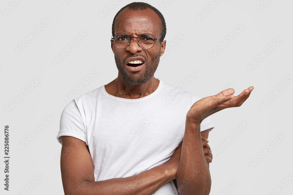 Annoyed young black man frowns face, shrugs shoulders, feels clueless as recieves unexpected bad proposal, dressed in casual t shirt, isolated over white background. Negative feelings concept Annoyed young black man frowns face, shrugs shoulders, feels clueless as recieves unexpected bad proposal, dressed in casual t shirt, isolated over white background. Negative feelings concept