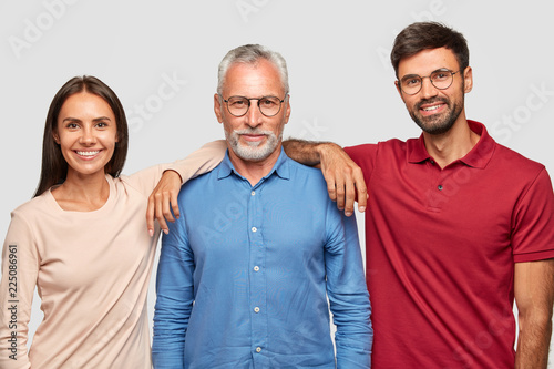 Multi generation concept. Family portrait of mature wrinkled man dressed in stylish shirt, stands between his daughter and son who came to congratulate him with anniversary, have good relationships