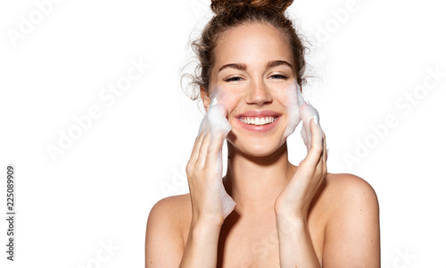 Portrait of young female with wetting face with foam. Cute girl posing in studio with bare shoulders. Beauty and skincare concept.