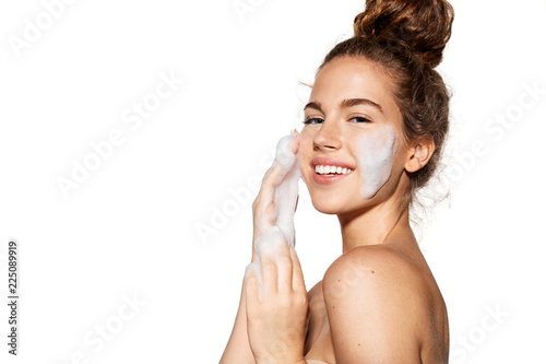 Portrait of young pretty girl with healthy skin on white background. Woman smiling and applying cosmetic foam on face.  Beauty skincare concept. photo