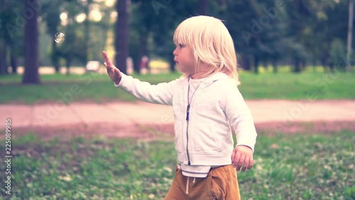 Happy child play with soap bubbles in spring park. Slow motion