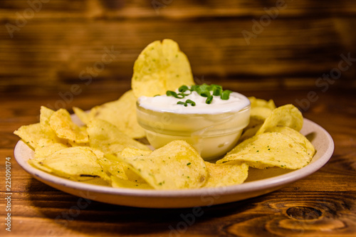 Ceramic plate with potato chips and glass bowl with sour cream on wooden table