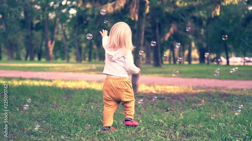 Happy child play with soap bubbles in spring park. Slow motion