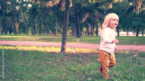 Happy child play with soap bubbles in spring park. Slow motion