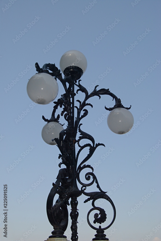 Candeeiro antigo com 4 pontos de luz - lampeão de rua em metal trabalhado com o céu de fundo e bolas brancas