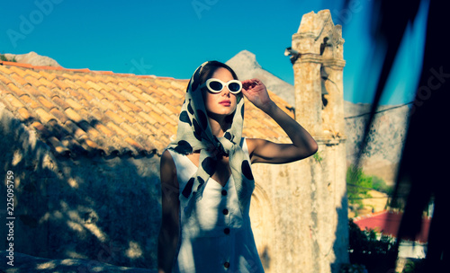 Fotografie Young girl dressing in 60s style clothes in a village with old church on background