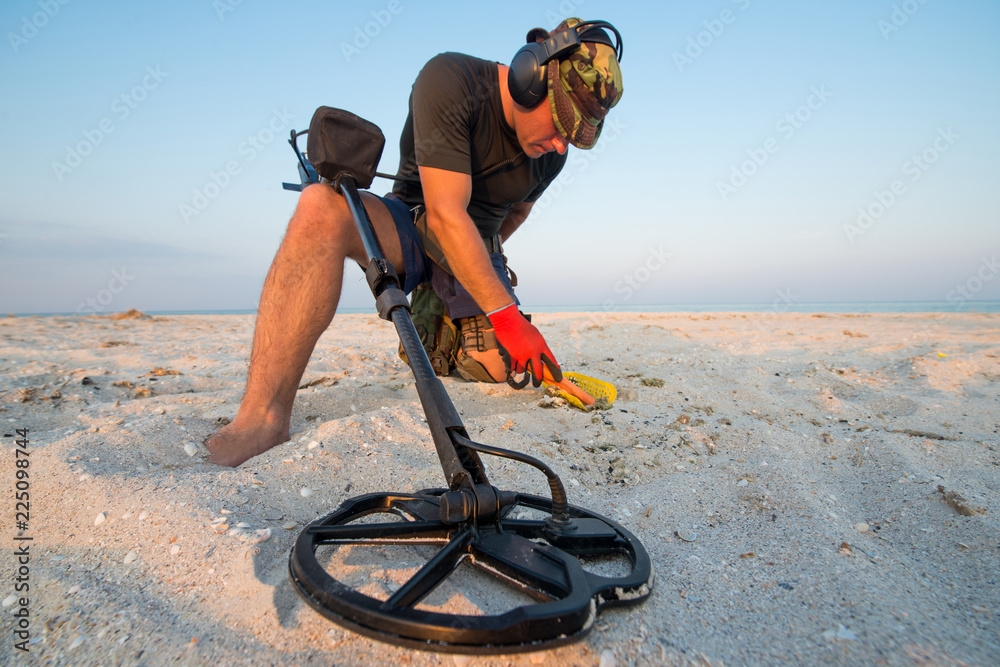 Man with a metal detector on a sea sandy beach - obrazy, fototapety, plakaty 