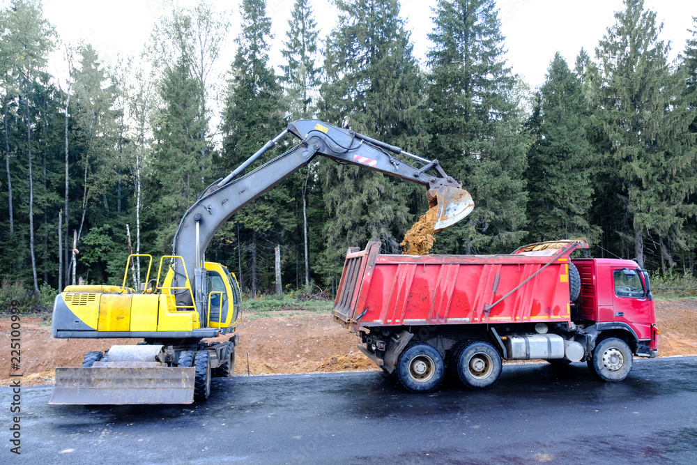 The wheel excavator loads the earth with a bucket to the body of a multi-ton dump truck on the construction site The wheel excavator loads the earth with a bucket to the body of a multi-ton dump truck on the construction site