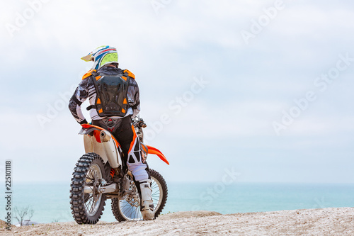 Fototapeta Naklejka Na Ścianę i Meble -  Motorcyclist in a protective suit sitting on motorbike in front of the sea