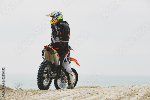 Motorcyclist in a protective suit sitting on motorbike in front of the sea
