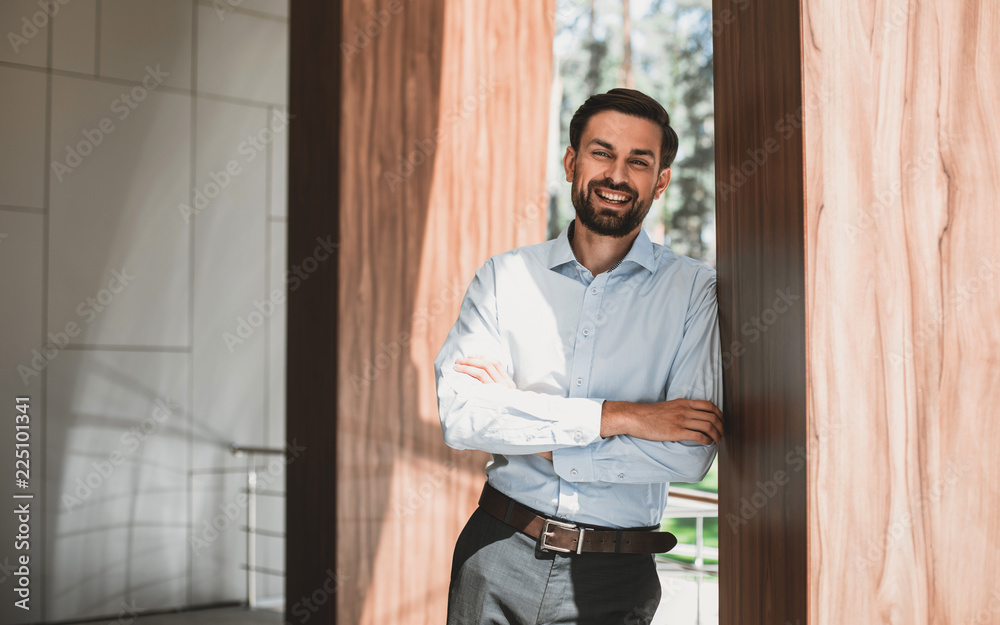 Waist up portrait of smiling man standing in light lobby. He is dressed in office wear and enjoying break in work. Copy space in left side