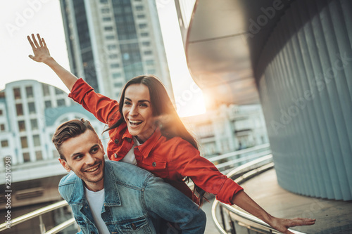Portrait of cheerful man having fun with positive girl while imitating plane with arms outdoor. Glad couple having fun together concept