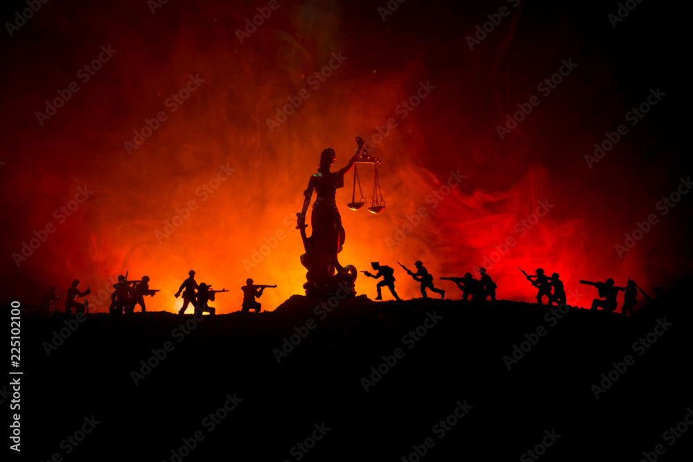 War - no justice concept. Military silhouettes fighting scene and The Statue of Justice on a dark toned foggy background.