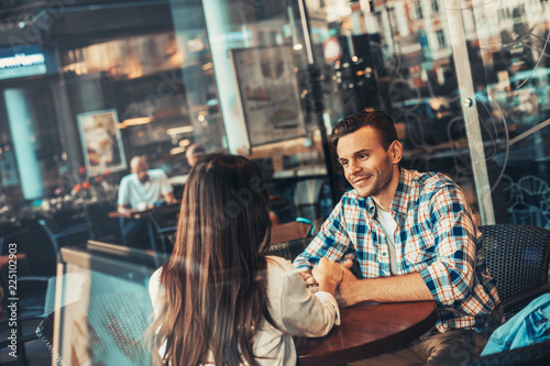 Positive male holding arm of woman while sitting at table in cozy cafe. Communication of glad couple concept