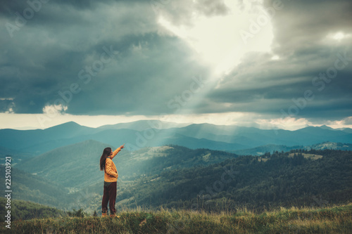 Pleasant active female traveler pointing the sky while enjoying mountain view