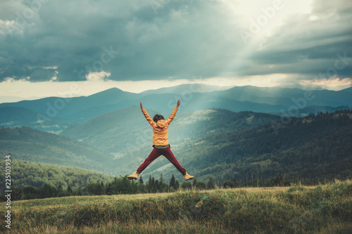 Joyful yougn woman jumping in the mountains while being impressed by beautiful scenary