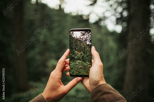 Perfect shot. Close up of mobile phone in arms of young lady isolated on blurred background. Woman taking picture of beautiful wood